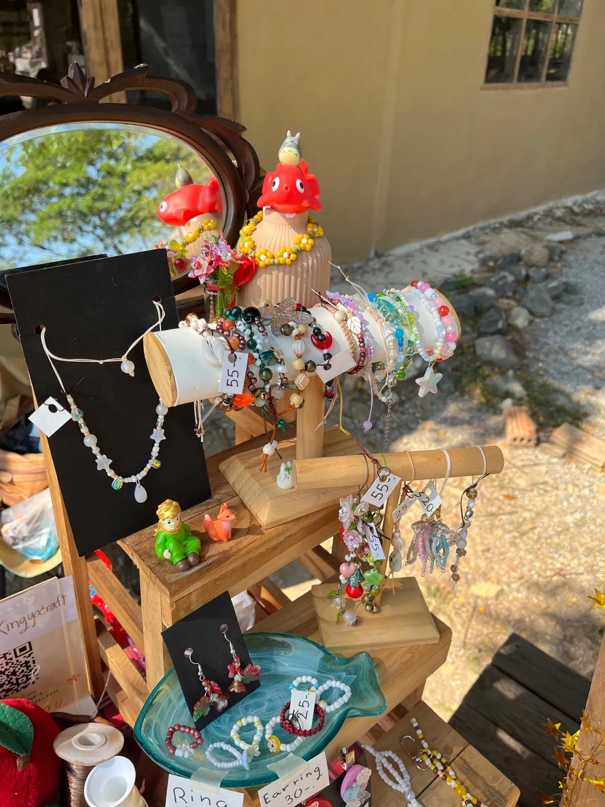 Outdoor display of handmade bead jewelry on a wooden stand.